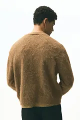 Cárdigan de punto marrón con textura peluda, cuello en V pronunciado y cierre frontal de botones. Presenta remates acanalados en puños y bajo, con un corte holgado.