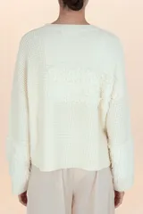 Suéter de punto color crema con diseño de paneles texturizados tipo peluche en el pecho y en los puños. Presenta cuello redondo y corte holgado.