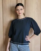 Remera negra de algodón con mangas abullonadas de textura diferenciada. Presenta costuras decorativas en color contrastante en el cuello y el ruedo.