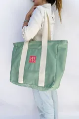 Bolso tote de tela canvas color crudo con asas largas a contratono color fucsia. Presenta un logo estampado al frente en color fucsia.