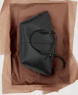 Bolso shopper negro de efecto piel, con dos asas de hombro, detalles metálicos, cierre de botón magnético y bolsillo interior con cremallera.