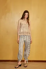 Pantalón bombacho de tiro medio con estampado de rayas verticales en tonos tierra y beige. Presenta aplicación de lentejuelas, cinturón del mismo tejido, forro interior tipo shorts y bajo acabado en puño con lazada. Cierre lateral con cremallera oculta.