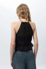 Top blanco sin mangas con cuello halter, bordado con calados y elástico con volado en la cintura.