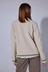 Saco tejido en lambswool con diseño de rombos y trenzas en el frente. Presenta cierre frontal con botones, cuello en V y detalles de rayas en contratono en puños y ruedo. Incluye pin bordado en la manga.