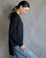 Buzo de tejido de punto en color gris claro, con cuello redondo, mangas largas con hombros caídos y diseño de corte asimétrico con la parte trasera más larga que la delantera.