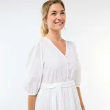Vestido corto blanco con diseño de bordado inglés, escote en V con botones frontales, mangas abullonadas tres cuartos y detalle de lazo ajustable en la cintura con falda escalonada.