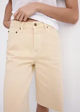 Bermuda de denim color amarillo pastel, de tiro bajo, corte recto y diseño de cinco bolsillos con cierre de botón y cremallera, y terminaciones deshilachadas.