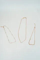 Set de tres collares dorados de diferentes largos y diseños: uno con bolitas espaciadas, otro liso y otro con dijes de flores.
