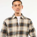 Camisa de manga larga con diseño de cuadros en tonos beige, negro y gris. Presenta cuello clásico, cierre frontal con botones y puños abotonados.