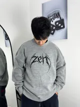 Sweater de punto color gris con diseño gráfico frontal estilo metalero en color negro. Presenta cuello redondo, mangas largas y corte oversize.