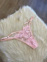 Tanga de encaje color rosa con diseño de tiras laterales regulables y detalle de elásticos.
