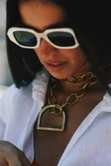 Collar plateado con cadena de eslabones grandes y dije dorado en forma de estribo.