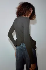 Jersey de punto gris oscuro con cuello redondo y manga larga, con bajo asimétrico acabado en volante con varilla metálica interior.