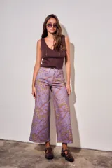 Pantalón jean de tiro alto y corte wide leg, con estampado de hojas grandes en tonos morados y fondo con patrón a cuadros.