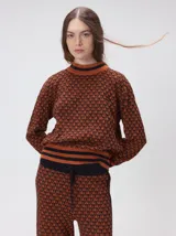 Sweater de punto jacquard con diseño geométrico en tonos naranja y negro, cuello alto tipo polera y puños acanalados.