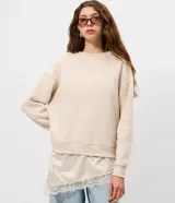 Buzo de algodón con felpa, corte oversized, cuello redondo y mangas largas. Presenta un detalle de encaje aplicado en el ruedo, aportando un contraste femenino y sofisticado.