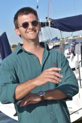 Camisa de manga larga, color verde azulado (verde inglés), con cuello camisero y botones frontales. Presenta un pequeño logo bordado en color rojo en el pecho. El tejido parece ser de lino o una mezcla ligera y arrugada.