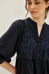 Vestido corto de viscosa color negro, con diseño holgado, mangas tres cuartos abullonadas y cuello en V. Presenta delicados bordados florales en tono azul oscuro en el pecho y en el ruedo, el cual termina con un borde festoneado.
