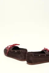 Mocasín tipo boat shoe color marrón, confeccionado en cuero, con cordones de cuero marrón y cordones decorativos azules.