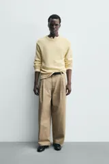 Pantalón chino de corte wide fit confeccionado en tejido de algodón. Presenta pliegues frontales, bolsillos laterales y bolsillos traseros de vivo, con cierre frontal de cremallera y botón.