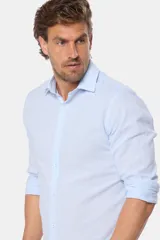 Camisa de manga larga, corte slim fit, color celeste con finas rayas verticales blancas. Presenta cuello camisero y un pequeño logo bordado en el pecho.