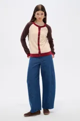 Cardigan de punto con diseño color block, presenta cuerpo en color celeste, mangas en color bordó y detalles de botones y bordes en color rosado. Posee cuello redondo y mangas largas.