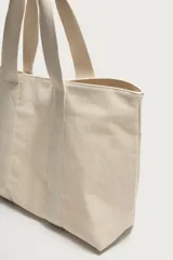 Bolso tipo shopper de tejido de algodón color beige, con doble asa de mano y cierre magnético.