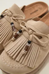 Suecos tipo mocasín color chocolate, confeccionados en material gamuzado. Presentan un diseño con flecos frontales, cordones decorativos con cuentas y una suela de plataforma plana de goma.