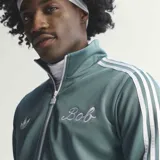 Campera deportiva Adidas Originals, modelo colaboración Bob Marley, color verde con las icónicas tres tiras blancas en las mangas. Presenta cuello alto, cierre frontal con cremallera y logo del Trifolio bordado en el pecho.