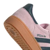 Championes adidas modelo Handball Spezial, confeccionados en gamuza color rosado con las icónicas tres tiras y detalle en el talón en color azul oscuro. Presentan una suela de goma color caramelo que aporta un estilo retro y distintivo.