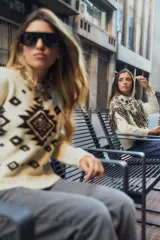 Sweater de lana color crudo con diseño geométrico en color marrón, cuello redondo y detalle de flecos en la parte frontal.