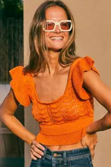 Top tejido de punto color naranja con destellos de lurex, escote redondo y mangas con volados. Presenta un diseño ajustado con cintura elástica acanalada.