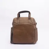 Mochila de diseño urbano en color caqui, confeccionada en cuero sintético con textura granulada y un bolsillo frontal de gamuza en tono más oscuro. Cuenta con manija superior, correas ajustables y bolsillos laterales.