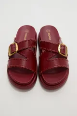 Sandalias planas de eco cuero color bordó, con tiras cruzadas y hebilla metálica dorada.