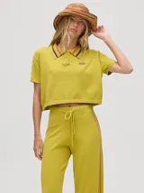 Chomba crop color beige, confeccionada en algodón, con cuello camisero que presenta rayas marrones y granates. Posee un pequeño logo bordado en el pecho.