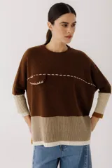 Buzo de tejido de punto con diseño color block en tonos marrón, beige y crema. Presenta un bolsillo pequeño en el pecho con detalle de costuras decorativas en hilo claro, cuello redondo y puños acanalados.