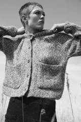 Chaqueta de punto de cuello redondo y manga larga, con textura jaspeada en tonos tierra y azul. Presenta cierre frontal con botones oscuros y dos bolsillos de plastrón en el delantero.