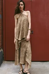 Top de cuello halter con tiras cruzadas para atar al cuello, hombros descubiertos y bajo asimétrico con caída drapeada y textura rústica con estampado sutil.