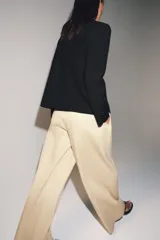 Pantalón de tiro medio con corte wide leg, confeccionado en algodón. Presenta cintura con trabillas, bolsillos laterales ocultos y detalle de pliegues en el delantero. Cierre frontal con cremallera, botón y ganchos metálicos.
