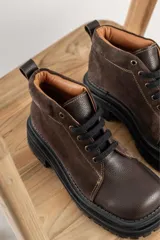 Borcegos de punta cuadrada con diseño acordonado, combinando paneles de cuero texturizado y gamuza en tonos marrones. Presentan una suela track gruesa de goma negra y cordones negros.