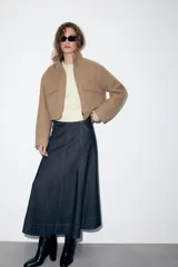 Falda midi de denim en color azul oscuro, con diseño evasé, bolsillos delanteros, costuras pespuntadas en contraste y cierre frontal con cremallera y botón metálico.