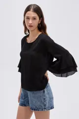 Blusa negra de poliéster, con cuello redondo, mangas 3/4 con volados en capas y diseño holgado.