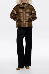 Chaqueta acolchada corta de tejido técnico color marrón, con cierre frontal de cremallera y botones a presión. Presenta capucha con borde de pelo sintético desmontable, bolsillos laterales con cremallera y puños elásticos.