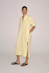 Vestido midi camisero de algodón, color amarillo con estampado a cuadros. Cuenta con cuello solapa, escote en V, mangas cortas con puño y bolsillos laterales ocultos en la costura, con diseño evasé.