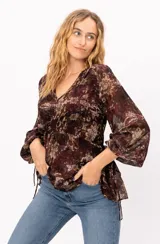 Blusa de gasa con estampado floral en tonos bordó y beige, de corte holgado, escote en V y mangas largas abullonadas. Presenta cordones laterales ajustables en el ruedo.