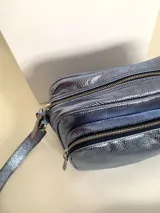 Bandolera rectangular de cuero azul metalizado con correa larga regulable. Cuenta con un bolsillo frontal con fuelle y un bolsillo trasero con cierre.