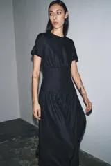 Vestido midi de denim color negro con cuello redondo y manga corta. Presenta un diseño con cintura entallada tipo bustier y falda con corte evasé. Cierre posterior con cremallera.