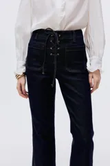 Jean de tiro alto en denim azul oscuro, con corte acampanado desde la rodilla. Presenta un diseño con cordones frontales para ajuste en la cintura, bolsillos delanteros y traseros, y costuras a contratono.