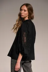 Camisa negra de corte holgado con cuello mao y escote en V. Presenta detalles de encaje en el cuello y en las mangas abullonadas de largo tres cuartos.