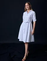 Vestido camisero blanco de algodón con cuello con solapa, delantera abotonada, mangas 3/4 regulables con presilla y botón, y cintura con lazo de ajuste.